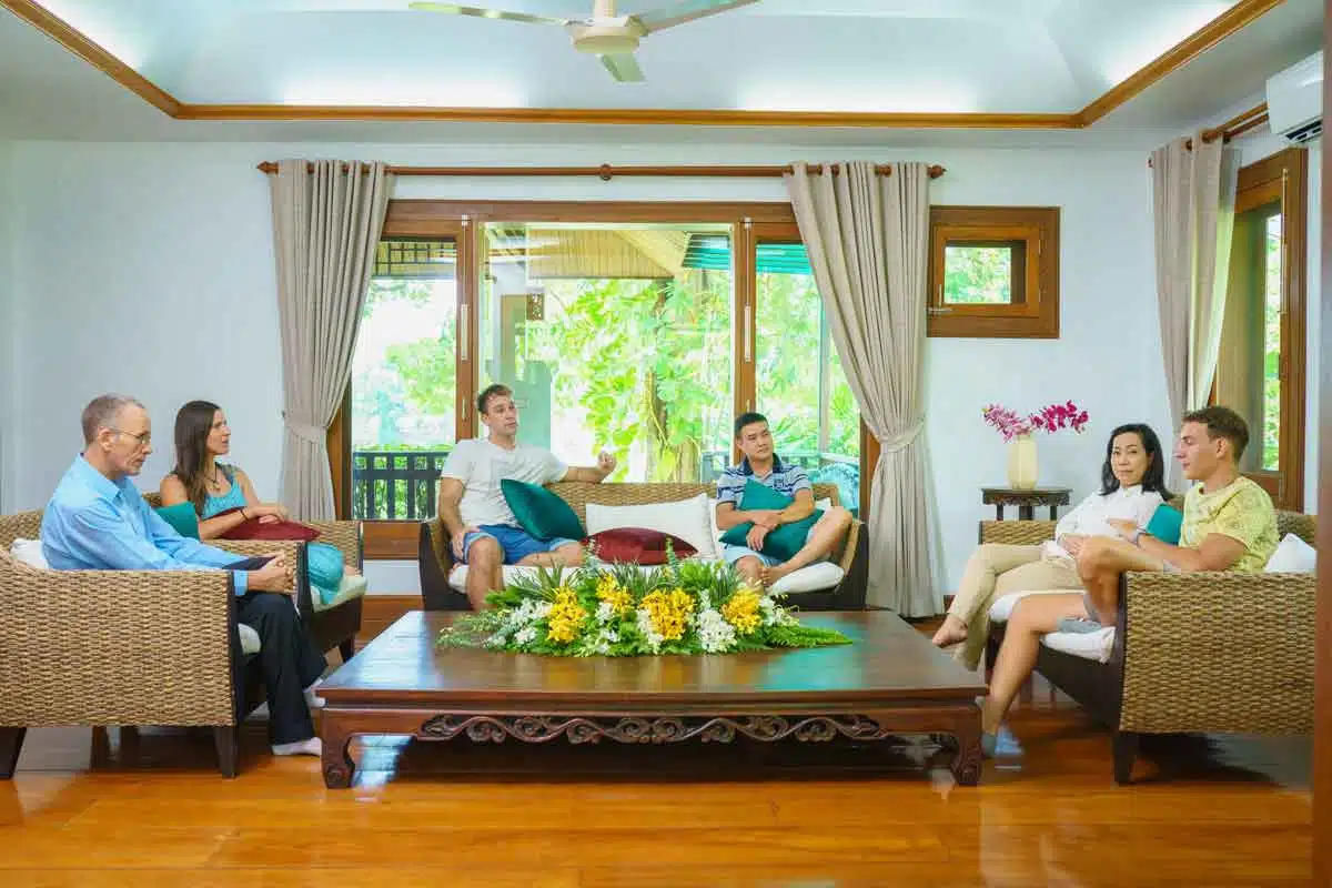 A group of six people engaged in a conversation seated indoors in a living room setting at The Dawn.