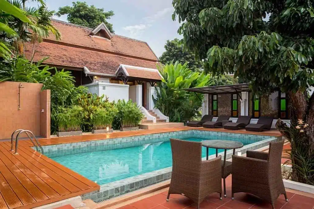 A pool area with lounge chairs and a wodden traditional building in the background at The Dawn.