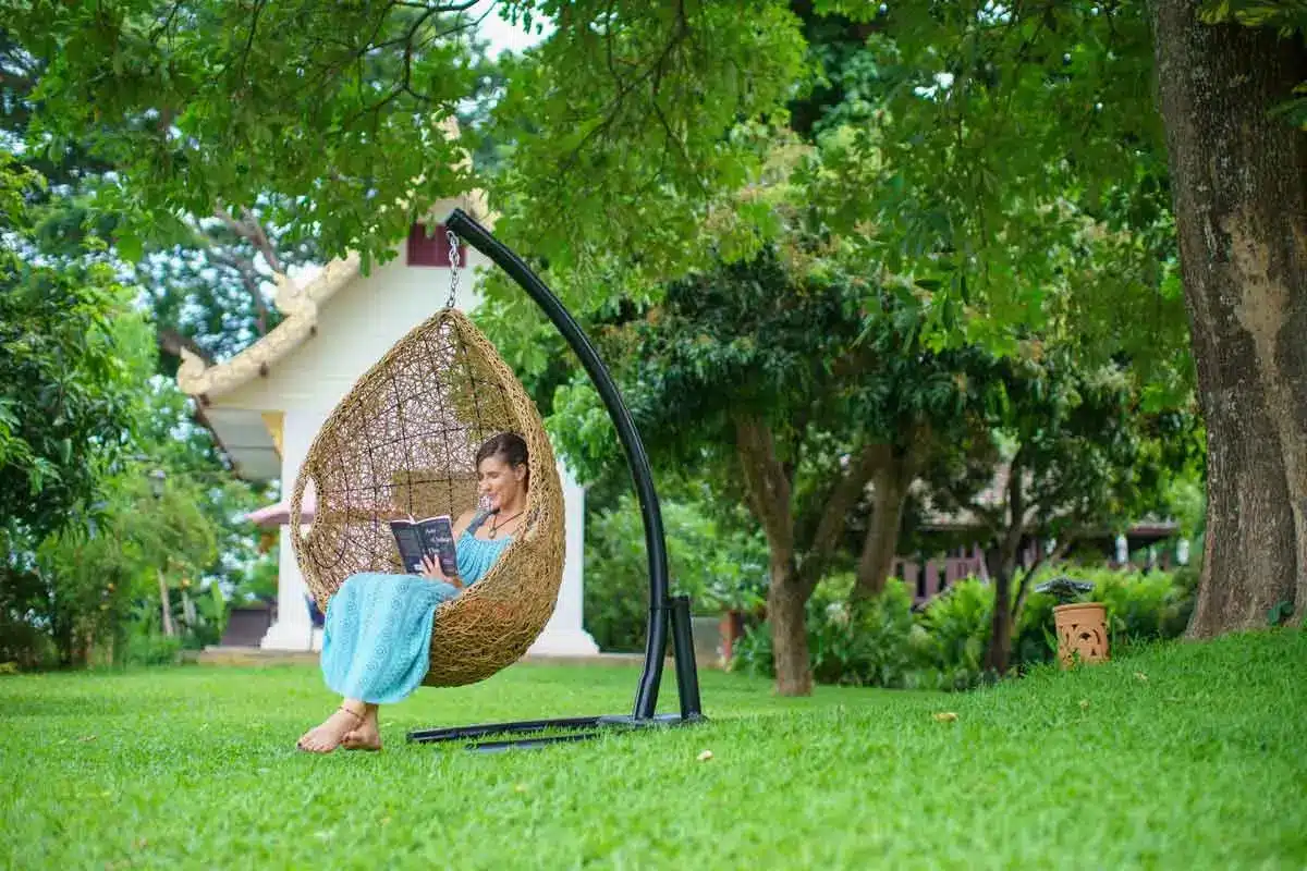 A woman relaxing with a book in a hanging chair surrounded by lush greenery at The Dawn.