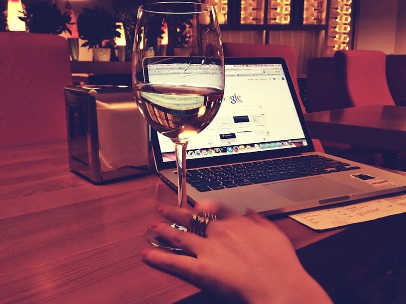Glass of white wine held in front of a laptop on a table