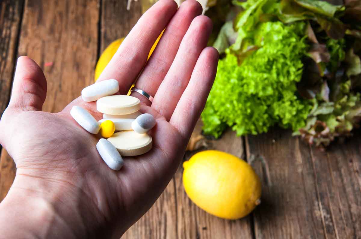 full hand of vitamins with vegetables and fruits in background