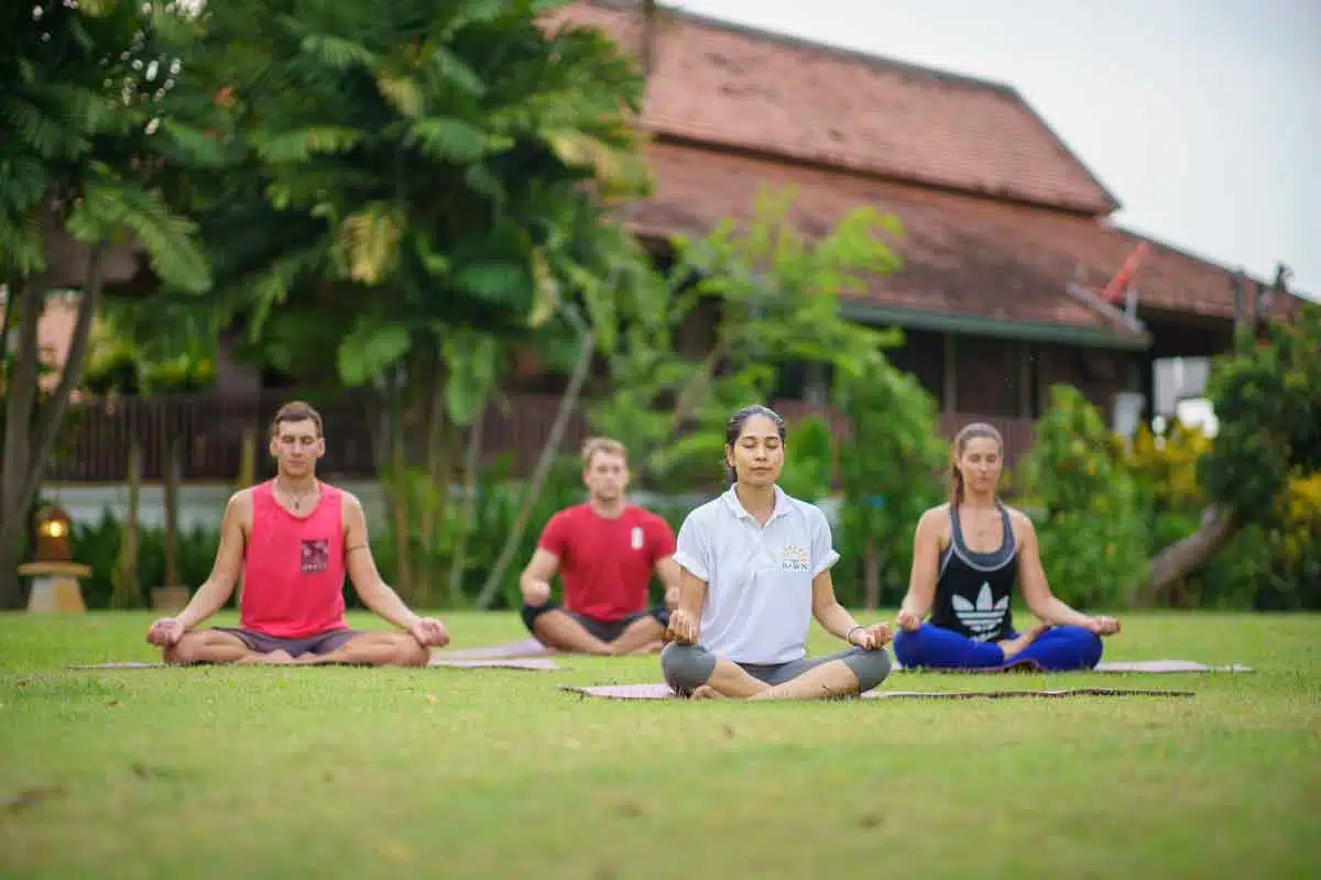 A group of four people meditating on yoga mats in a garden at The Dawn.