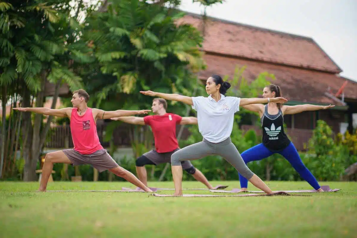 A group of four people practicing the Warrior II yoga pose on a lawn at The Dawn.