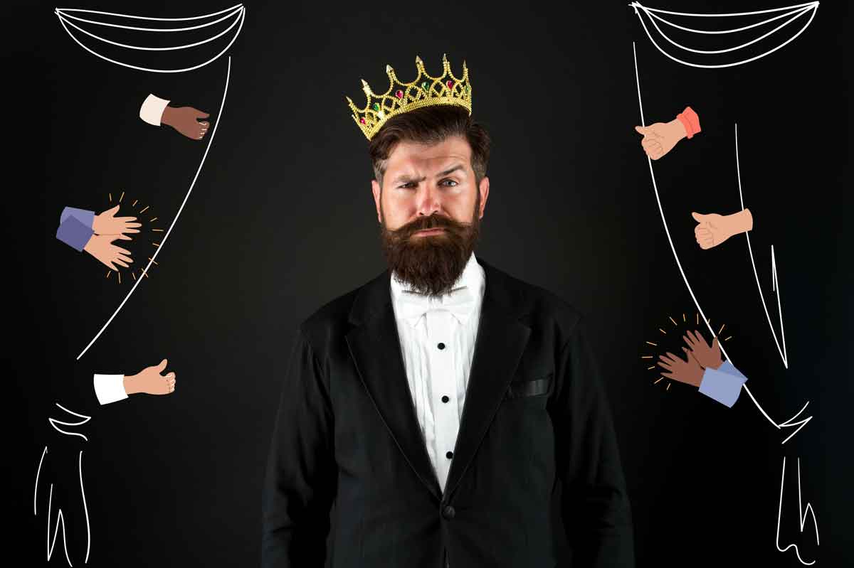 Bearded man in a tuxedo wearing a crown, surrounded by illustrated applauding hands