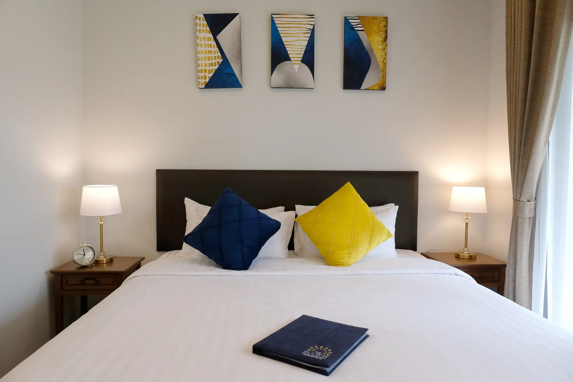 A photo of The Dawn's bedroom that has a comfortable bed covered in white sheets with blue and yellow pillows.