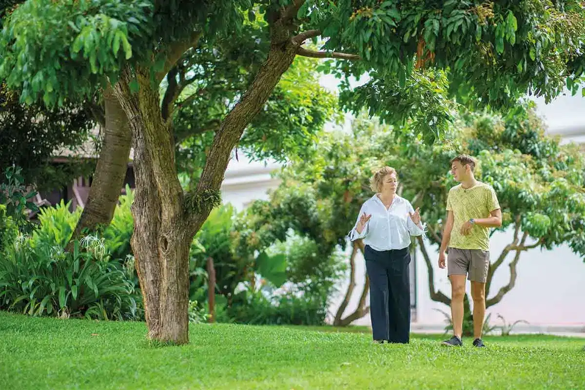 Two people walking and talking in a garden under a large tree at The Dawn.