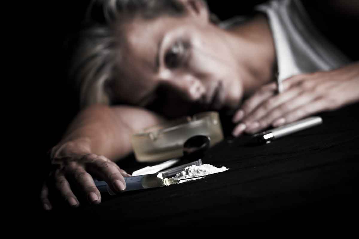 Drug-addicted woman holding a syringe next to a small pile of white powder